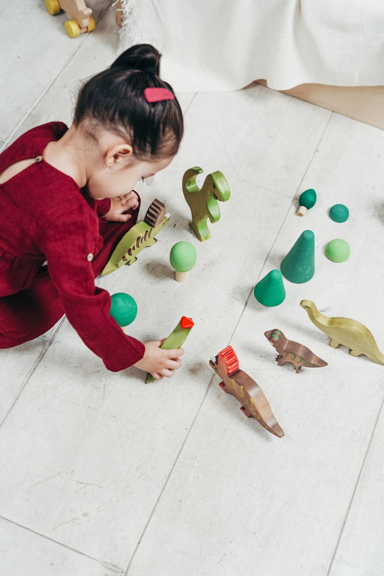 A child in red dress playing with wooden dinosaur toys indoors, sparking creativity and imagination.