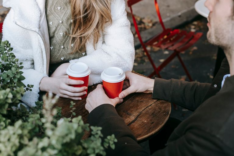 High angle of crop faceless woman sitting with boyfriend in modern street cafe and drinking coffee on autumn day