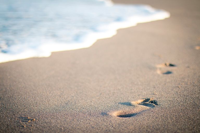 Close-up of footprints on a sandy beach with gentle waves in Marbella, Spain.
