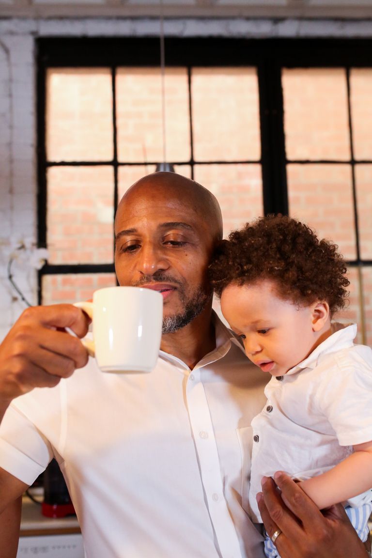 A father holds his son while enjoying a hot beverage in a cozy indoor setting.