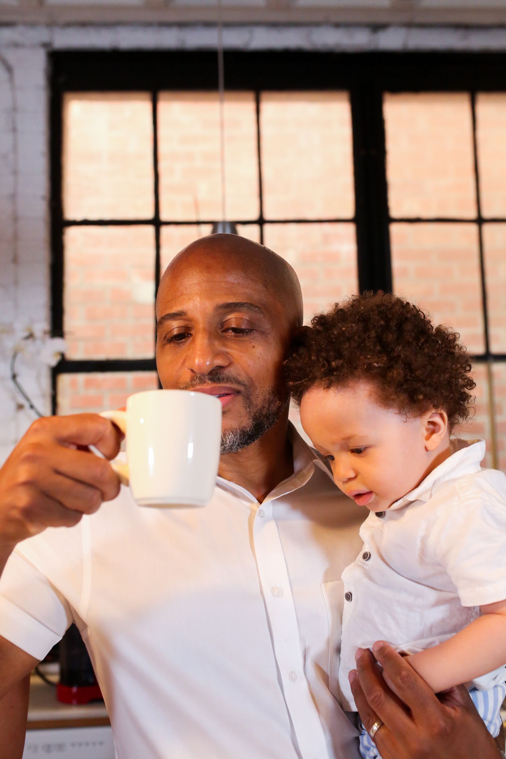 A father holds his son while enjoying a hot beverage in a cozy indoor setting.