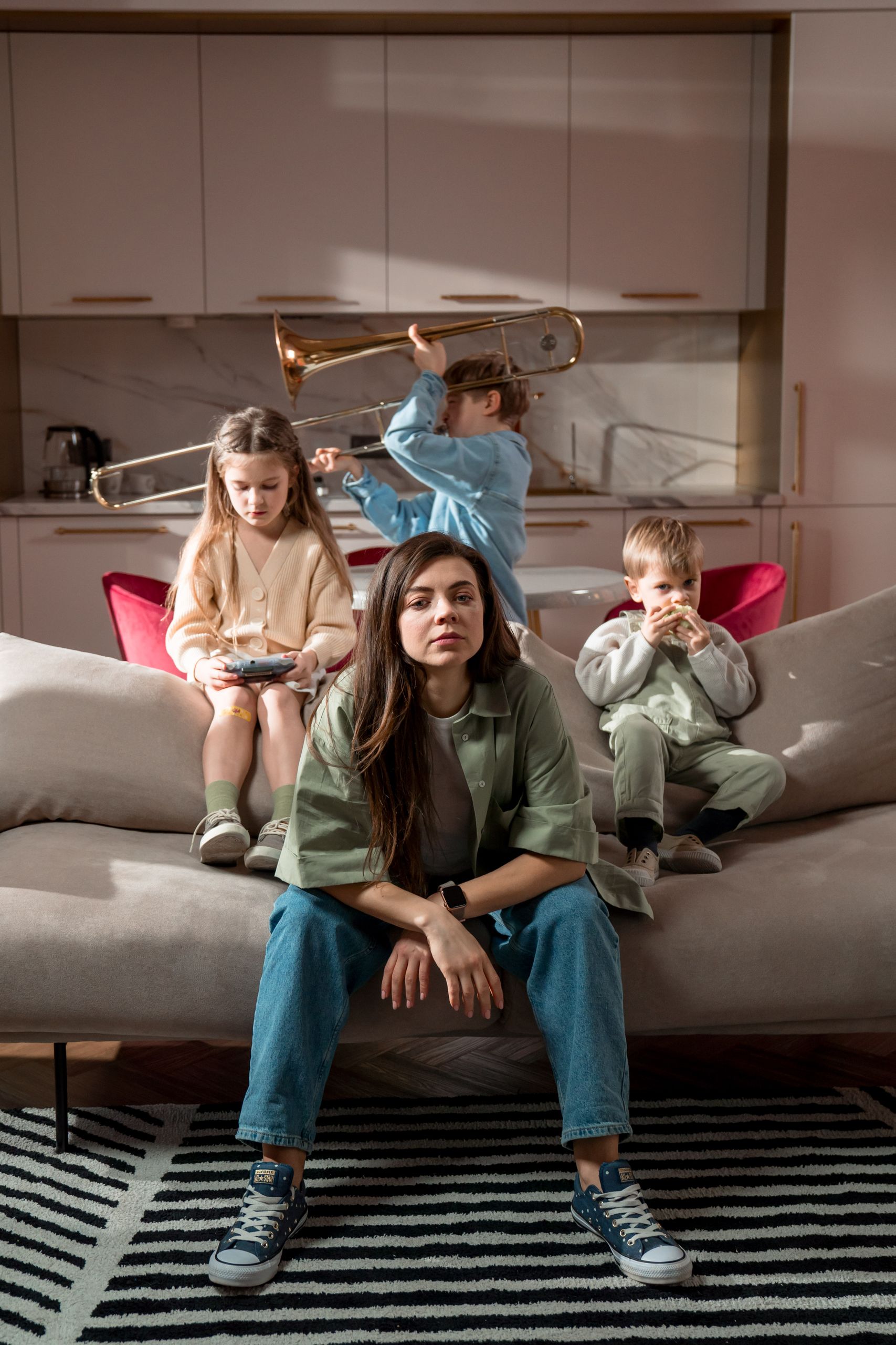 A mother sits with her children playing indoors on a sofa in a modern living room.